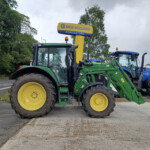 Two green New Holland tractors with yellow wheels parked in a lot under a yellow New Holland Agriculture sign.