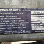 Close-up of a weathered metal nameplate with multilingual labels for a liquid manure spreader, showing serial number and year of manufacture.