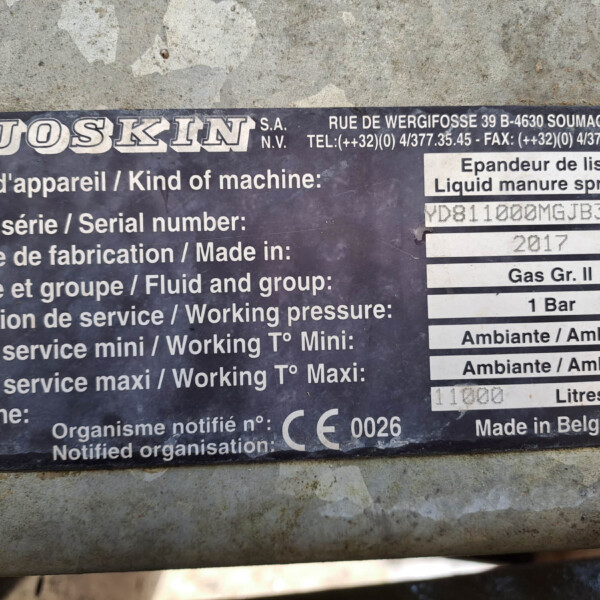 Close-up of a weathered metal nameplate with multilingual labels for a liquid manure spreader, showing serial number and year of manufacture.