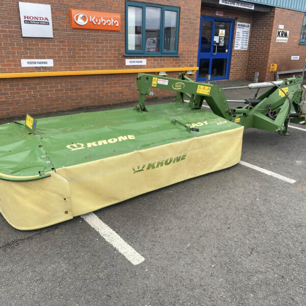 Green Krone mower in a parking lot outside a brick building with Honda and Kubota signs and a blue door.