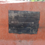 Close-up of a dirty black identification plate on an orange machine, showing KUHN S.A. and 'Made in France' text.