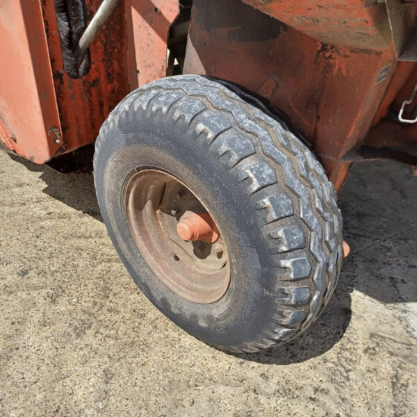 Close-up of a rugged off-road tire on an orange construction machine, dirt on the ground.