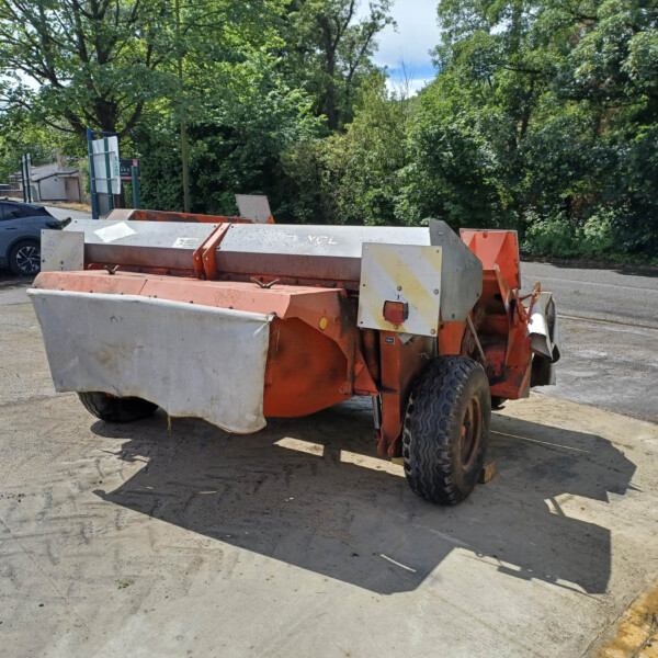 Orange construction trailer with metal panels and wheels parked on a paved lot, with green trees in the background.