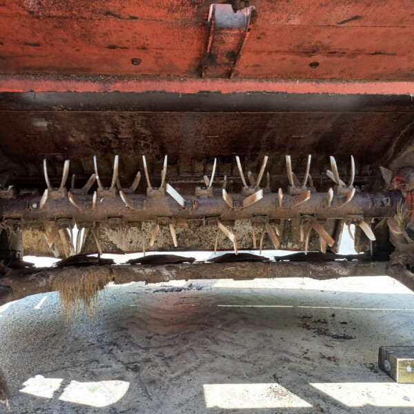 Rusty red agricultural implement with curved metal tines arranged in a row beneath the frame