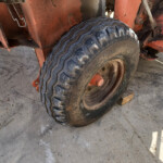 Close-up of a rugged tire on a rusty orange farm trailer, on a concrete floor.