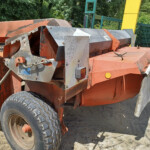 Orange heavy machinery with exposed metal components and cracked paint outdoors; large tires visible at bottom left.