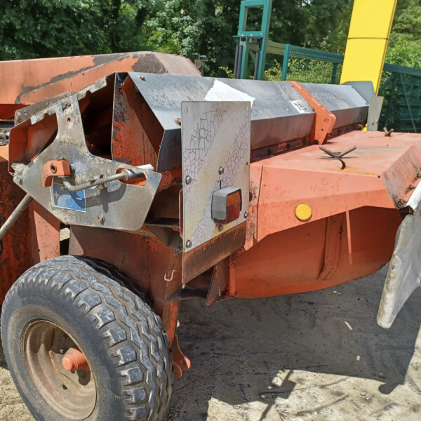 Orange heavy machinery with exposed metal components and cracked paint outdoors; large tires visible at bottom left.