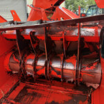 Close-up of red agricultural harvester header blades and feed mechanism with dirt and straw residue inside the machine