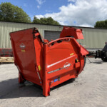 Red KUHN Primor 2060 M feed mixer in an outdoor equipment yard with pallets and a beige metal building behind.