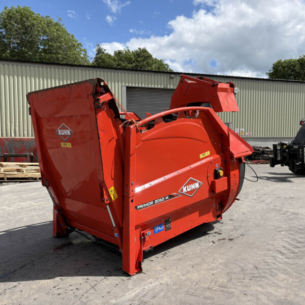 Red KUHN Primor 2060 M feed mixer in an outdoor equipment yard with pallets and a beige metal building behind.