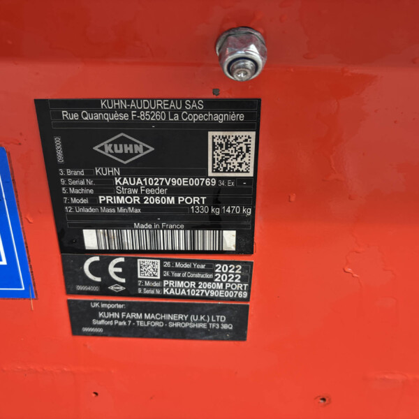 Close-up of a red machine with a black identification plate showing KUHN branding, a barcode and QR code, and model/serial details partially visible.