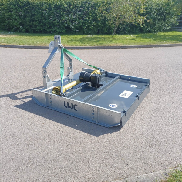 Metal platform/trailer base on a paved surface, secured with green ratchet straps, with grass and bushes in the background.