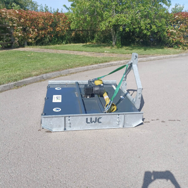 Metal trailer hitch with green straps on a paved road, a grassy curb and flowering hedge in the background.