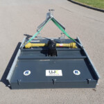 Top-down view of a gray trailer carrying industrial equipment, with a yellow hydraulic unit and green securing straps on a paved surface