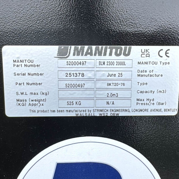 Close-up of a metal data plate on a black surface showing MANITOU branding, part numbers, serial number 251378, date June 25, and capacity 2.0 m3.
