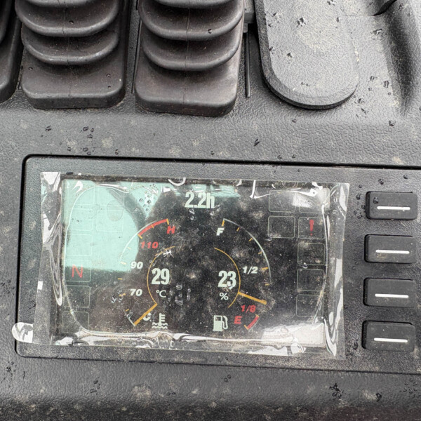 Close-up of a car's instrument cluster under a rain-speckled dashboard, showing temperature and fuel gauges.