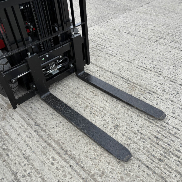 Close-up of black forklift forks extending over a textured concrete surface, with part of the forklift frame visible.