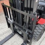 Close-up of a forklift mast with forks and chain drive against a brick wall behind.