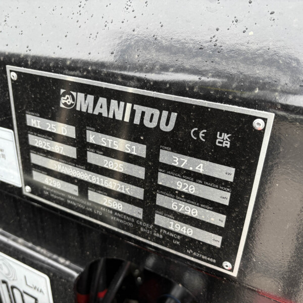 Metal nameplate on a rugged machine showing the Manitou logo and model/serial data, partially wet with raindrops.
