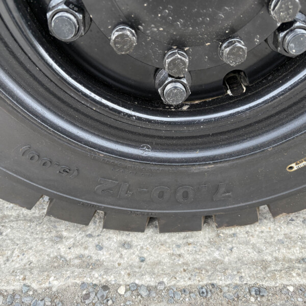 Close-up of five lug nuts securing a black wheel hub, with a dirty tire and gravel ground visible around it.