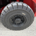 Close-up of a large rugged tire on a red heavy-duty vehicle, standing on a concrete surface.