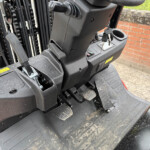 Forklift operator area with ignition keys in the console, pedals underfoot, and control panel nearby.