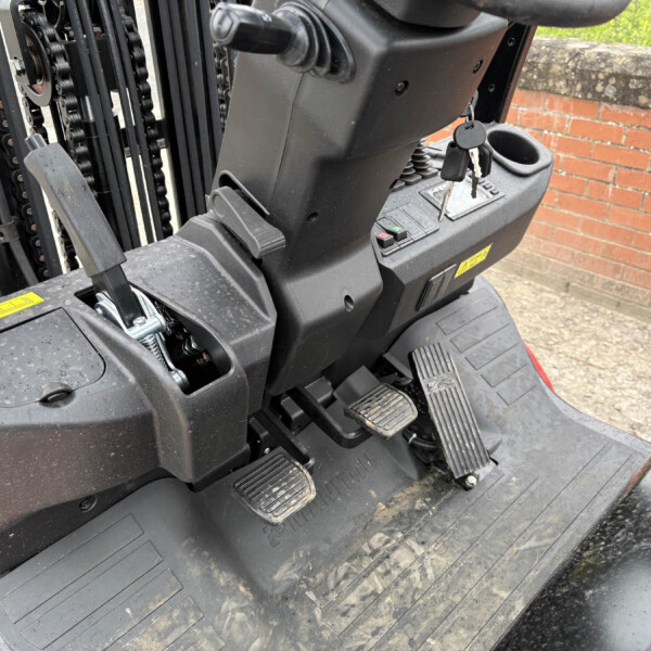 Forklift operator area with ignition keys in the console, pedals underfoot, and control panel nearby.