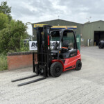 Red Manitou forklift with extended forks in front of a green warehouse labeled Russell's, outdoor industrial yard.