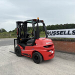 Red Manitou forklift parked in front of a brick wall and Russell's sign in an outdoor lot.