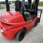 Red Manitou MI25D forklift with black mast and operator seat, parked on a gravel industrial yard.