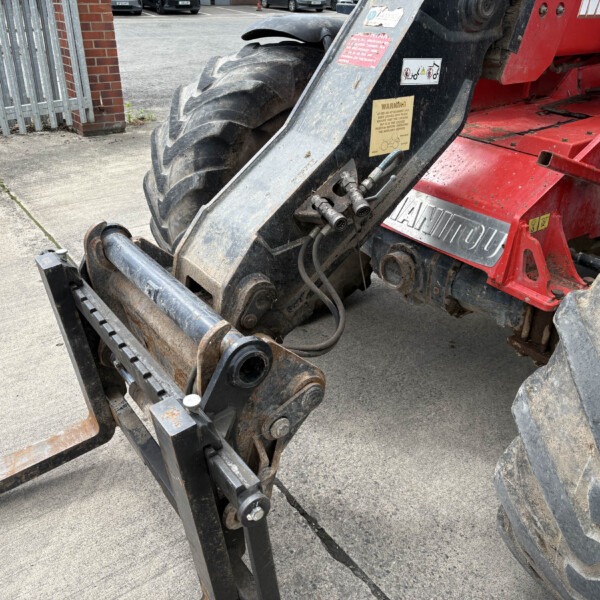 Close-up of a red construction machine's hydraulic attachment and large worn tires on a concrete surface.
