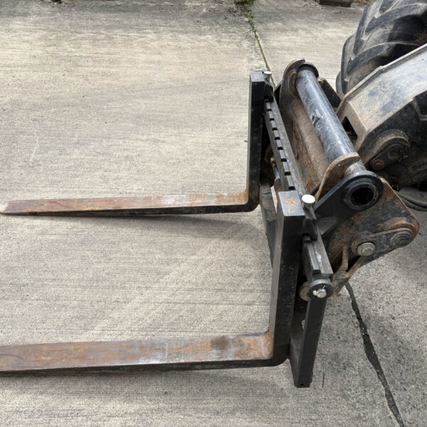 Rusty forklift forks extended forward over a worn concrete surface, with part of the hydraulic lift on the right side.