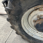 Close-up of a large tire and rusted wheel on a heavy vehicle, with a dirty ground surface nearby.