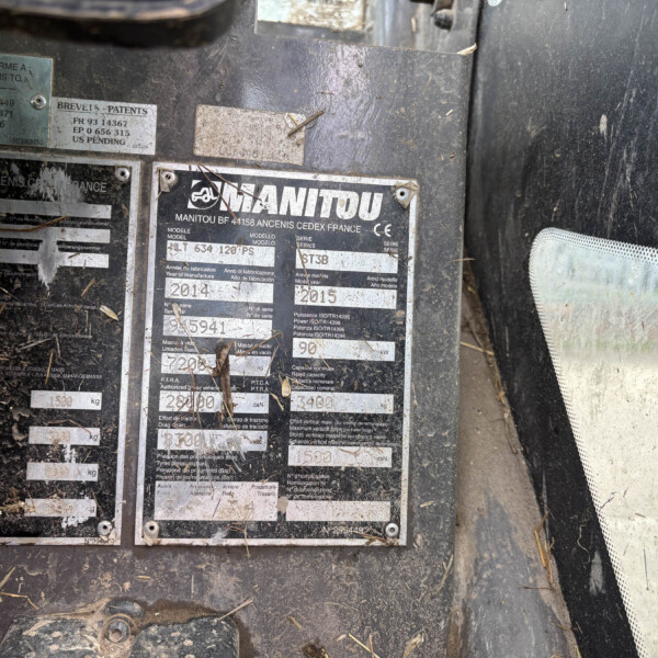 Close-up of a dirty metal identification plate on heavy equipment, showing the MANITOU branding and model/year labels.