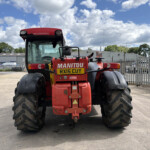 Back view of a red Manitou telehandler in an industrial yard, large tires, and a yellow license plate RX15 CUY.
