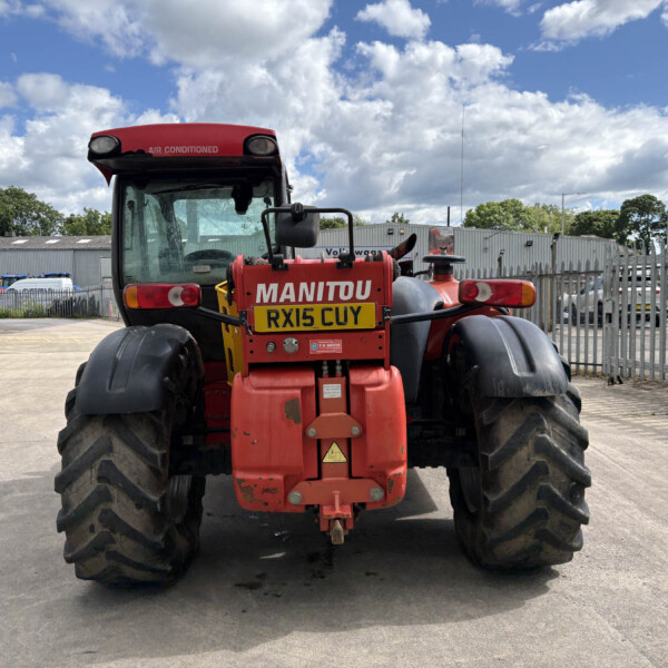 Back view of a red Manitou telehandler in an industrial yard, large tires, and a yellow license plate RX15 CUY.