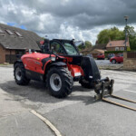 Red agricultural tractor with a front loader parked in a residential parking lot, cloudy sky overhead.