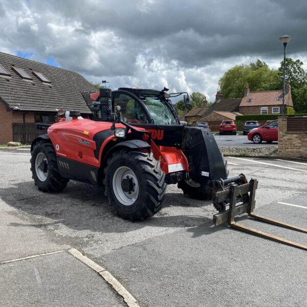 Red agricultural tractor with a front loader parked in a residential parking lot, cloudy sky overhead.