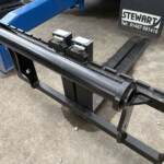 Close-up of forklift pallet forks attached to a blue frame on a concrete floor.