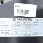 Close-up of identification labels on a dark metal surface; shows Manitou branding and part/serial numbers with a barcode.