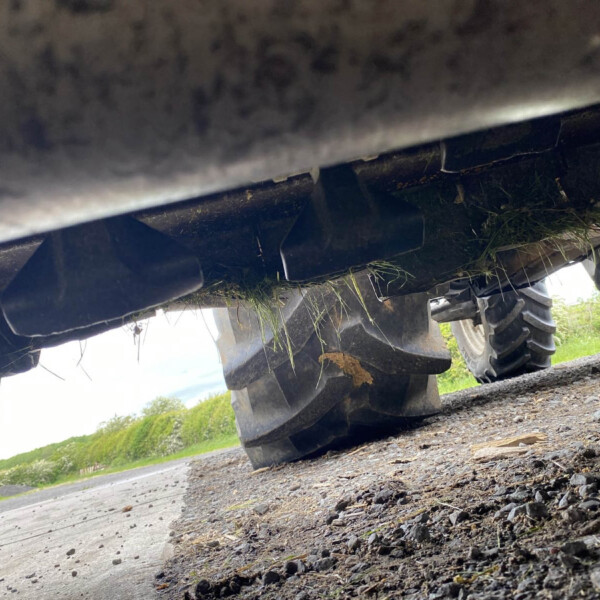 Underneath a heavy vehicle, showing a tire and the undercarriage with grass stuck to it on a gravel road.