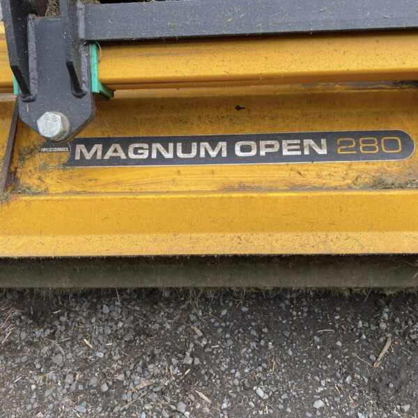 Close-up of a yellow Magnum Open 280 agricultural implement with a black mounting bracket and a large bolt, on a gravel surface.