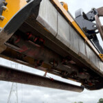 Close-up of heavy construction machinery with yellow-painted beams, bolts, and rusted steel components.