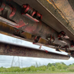 Close-up of rusted red hydraulic machinery components under heavy construction equipment.