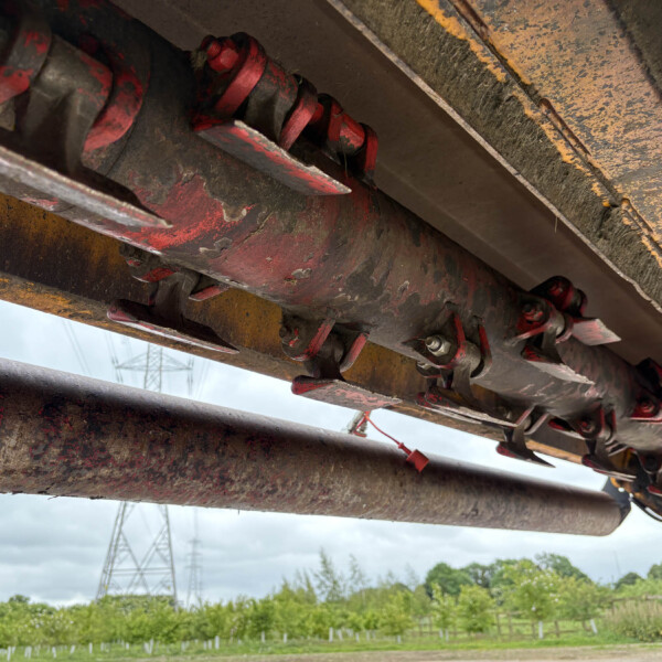 Close-up of rusted red hydraulic machinery components under heavy construction equipment.