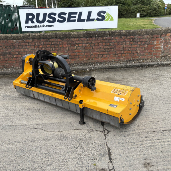 Yellow industrial attachment on a paved surface in front of a red brick wall and a Russell sign/screen in the background