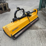 Yellow Magnum Elite 225 plate compactor attachment on a concrete surface beside a rusty forklift frame and brick wall in the background.