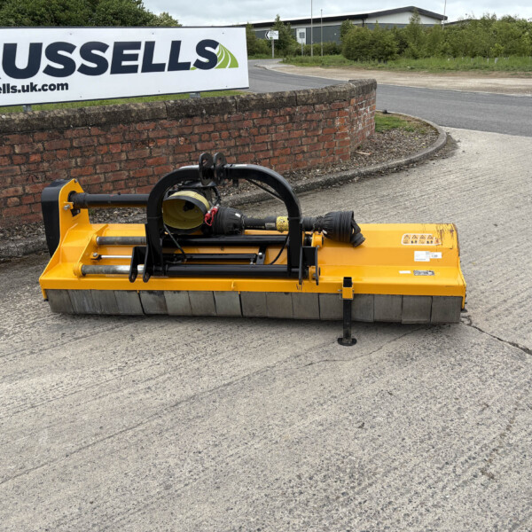 Yellow street-sweeper/brush attachment on a paved road next to a brick wall and a Russell's sign in the background.