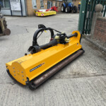 Yellow Magnum Elite 225 industrial machine with hydraulic arms, in a yard with tractors and a rusty forklift in the background.