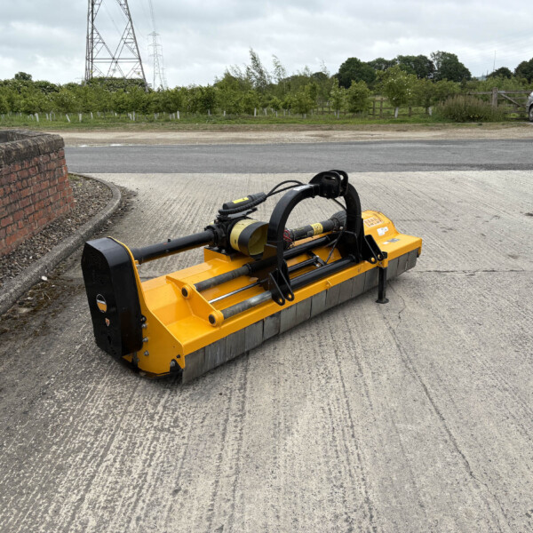 Yellow street-sweeper attachment parked on a paved road beside a brick wall, with a sign, a silver car, and trees in the background.